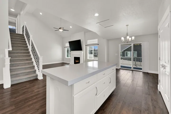 Open-concept living area featuring a large kitchen island with a light-toned countertop, wood-finish flooring, a fireplace with a mantel, and a staircase with white balusters and dark metal spindles