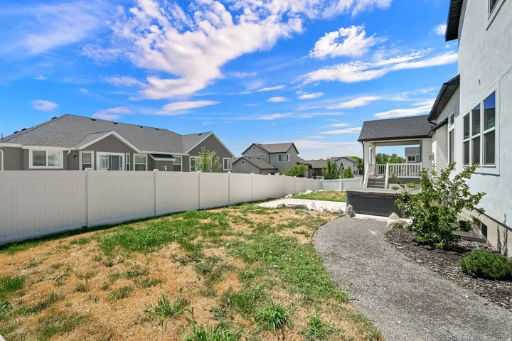 Backyard featuring a covered deck with white railings, a gravel pathway, and a privacy fence