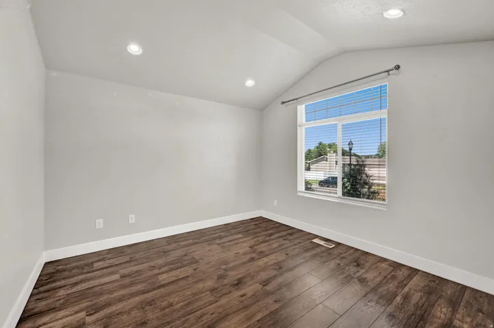 Room featuring a vaulted ceiling with recessed lighting, wood-finish flooring, and a large window with blinds