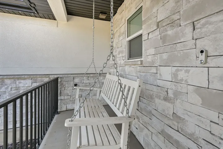 Front porch featuring a white porch swing, textured stucco siding, and stacked stone accents