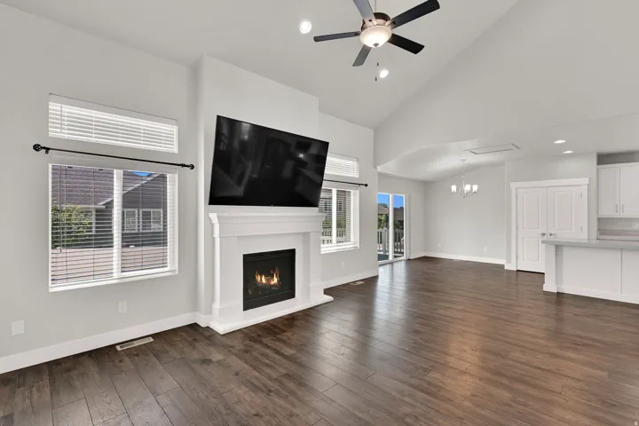 Spacious living area featuring vaulted ceilings, wood-finish flooring, a white mantel fireplace, and a ceiling fan with integrated lighting