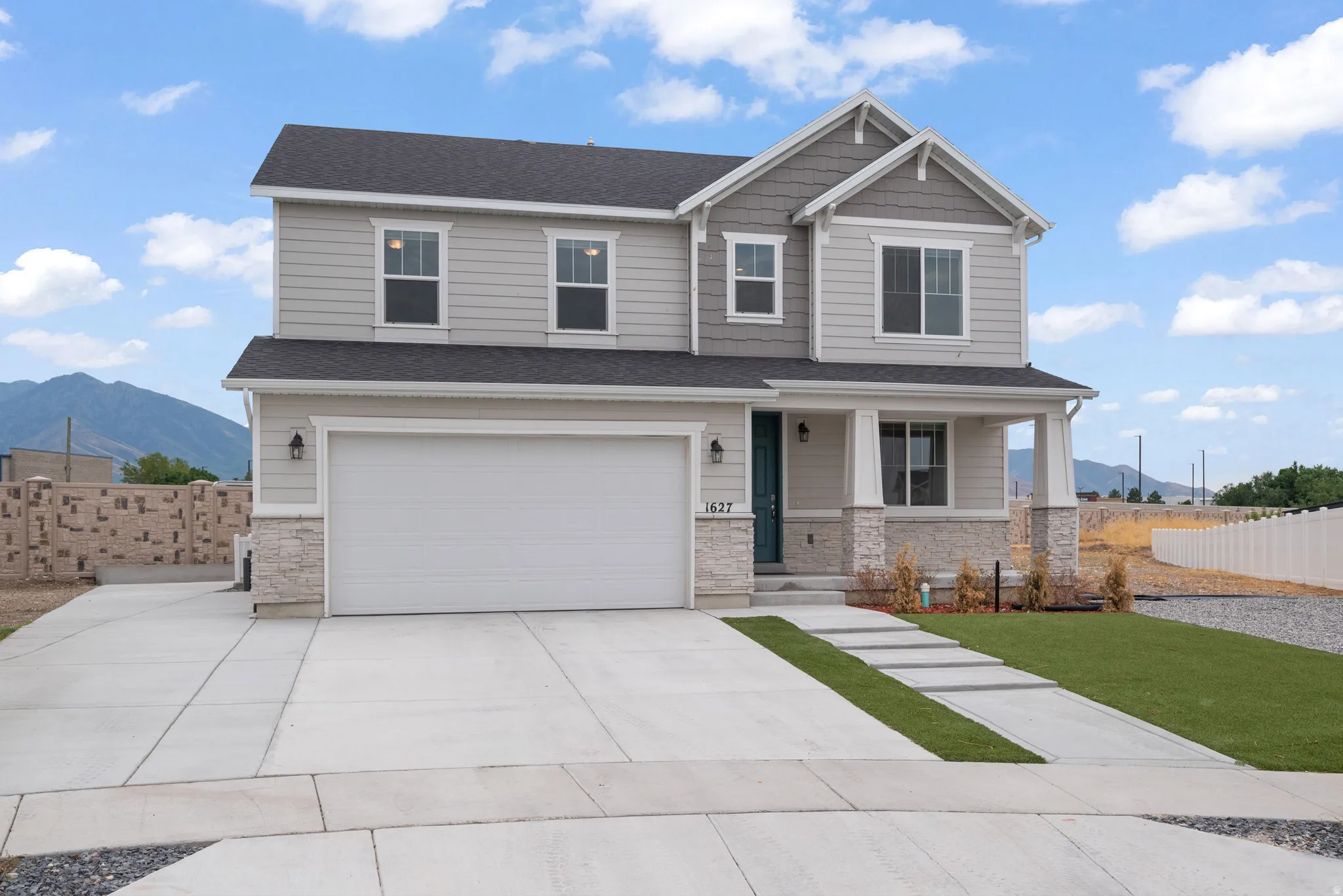 Two-story residence featuring light gray siding with stone veneer accents, a dark asphalt shingle roof, and an integrated two-car garage