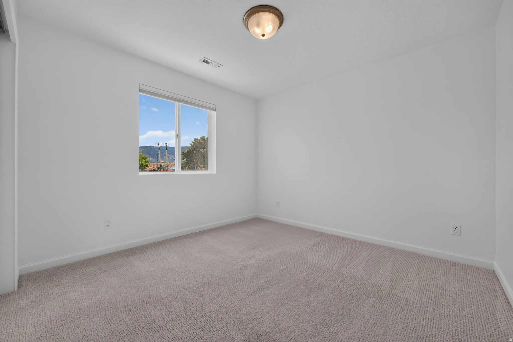 Bedroom featuring neutral carpeting, white walls, and a window providing natural light and a distant mountain backdrop
