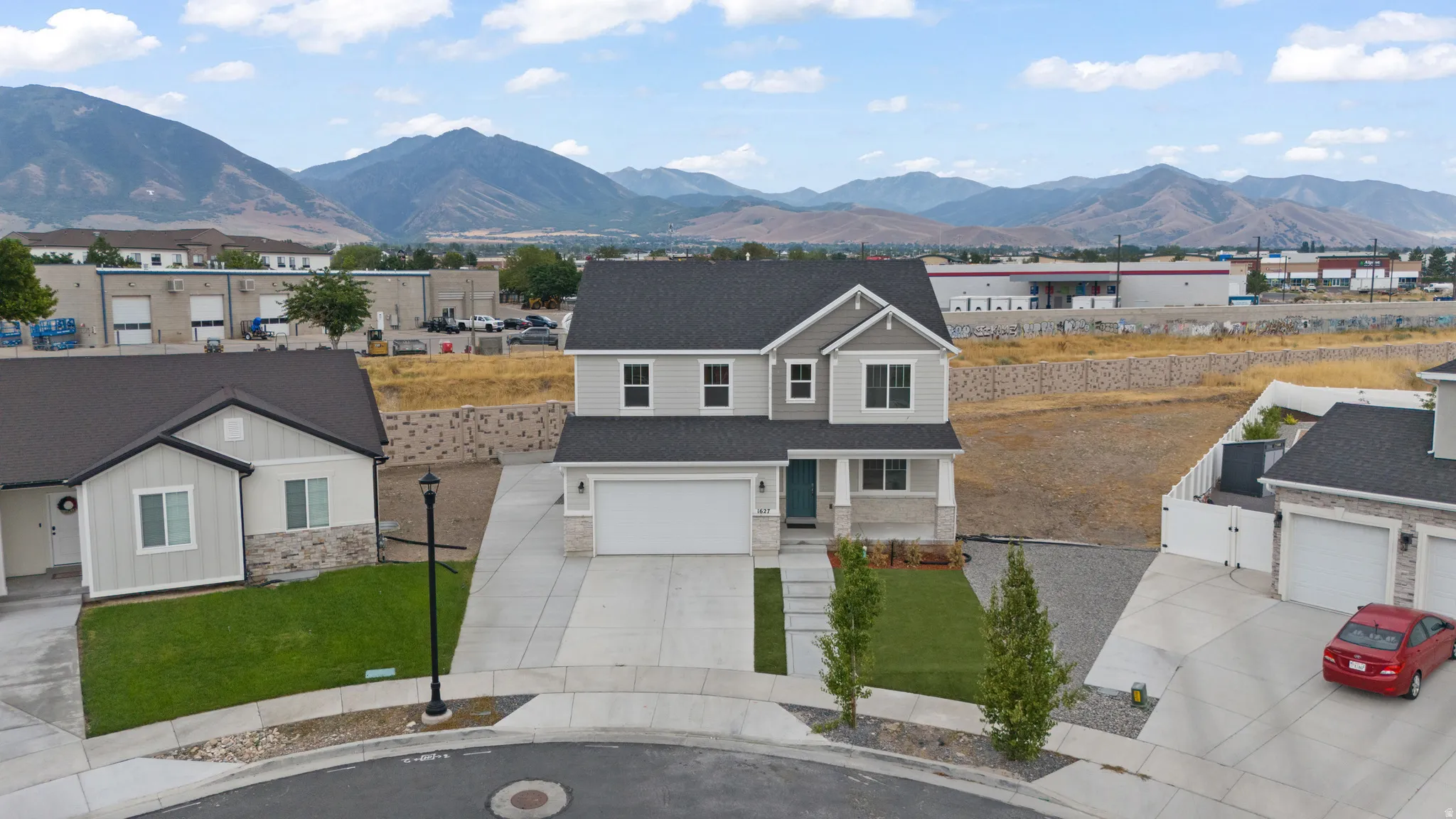 Two-story residence featuring light gray siding with stone-look accents, a dark shingled roof, and a two-car garage