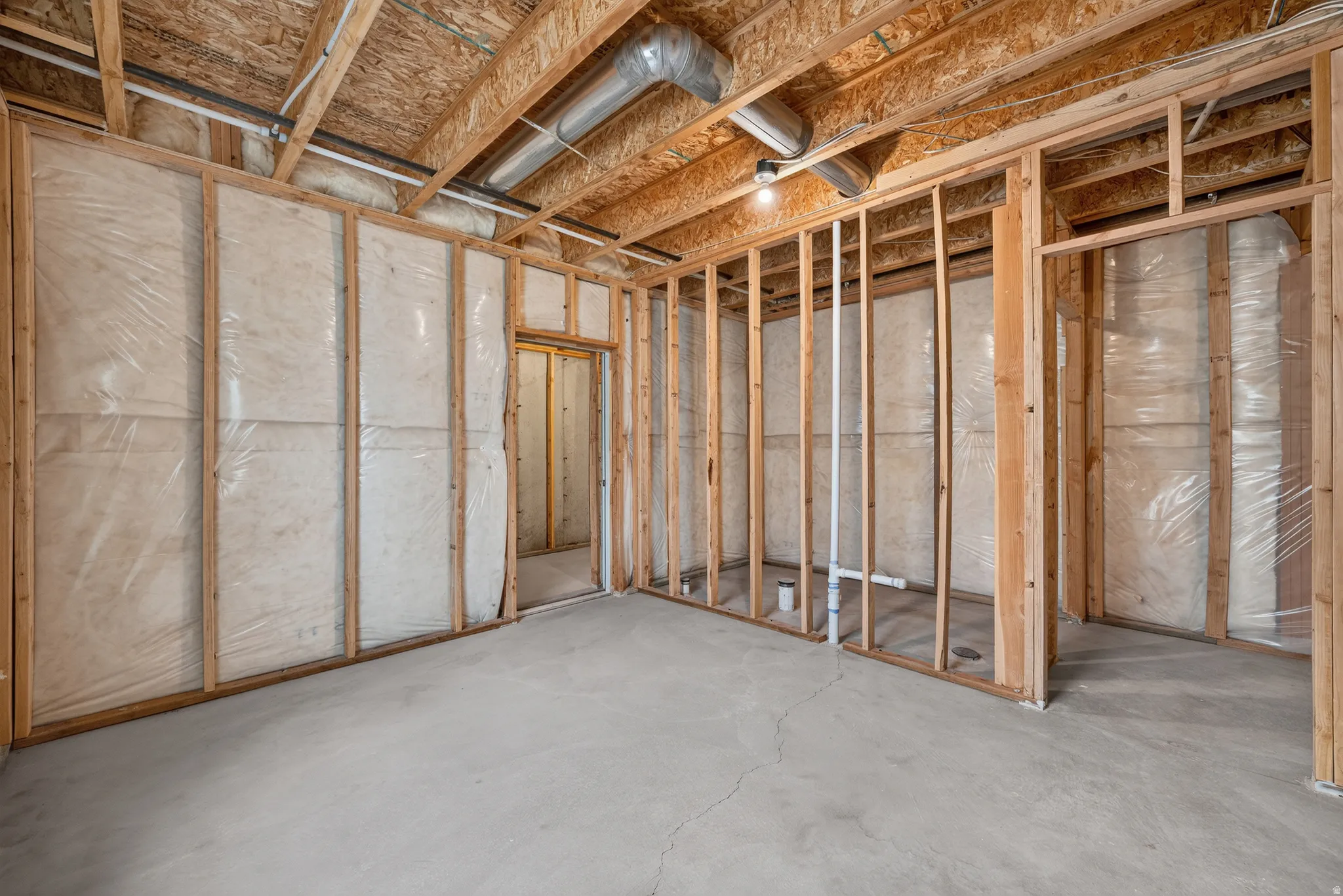Unfinished basement space featuring exposed wooden framing, concrete flooring, insulation with vapor barrier, and exposed ductwork