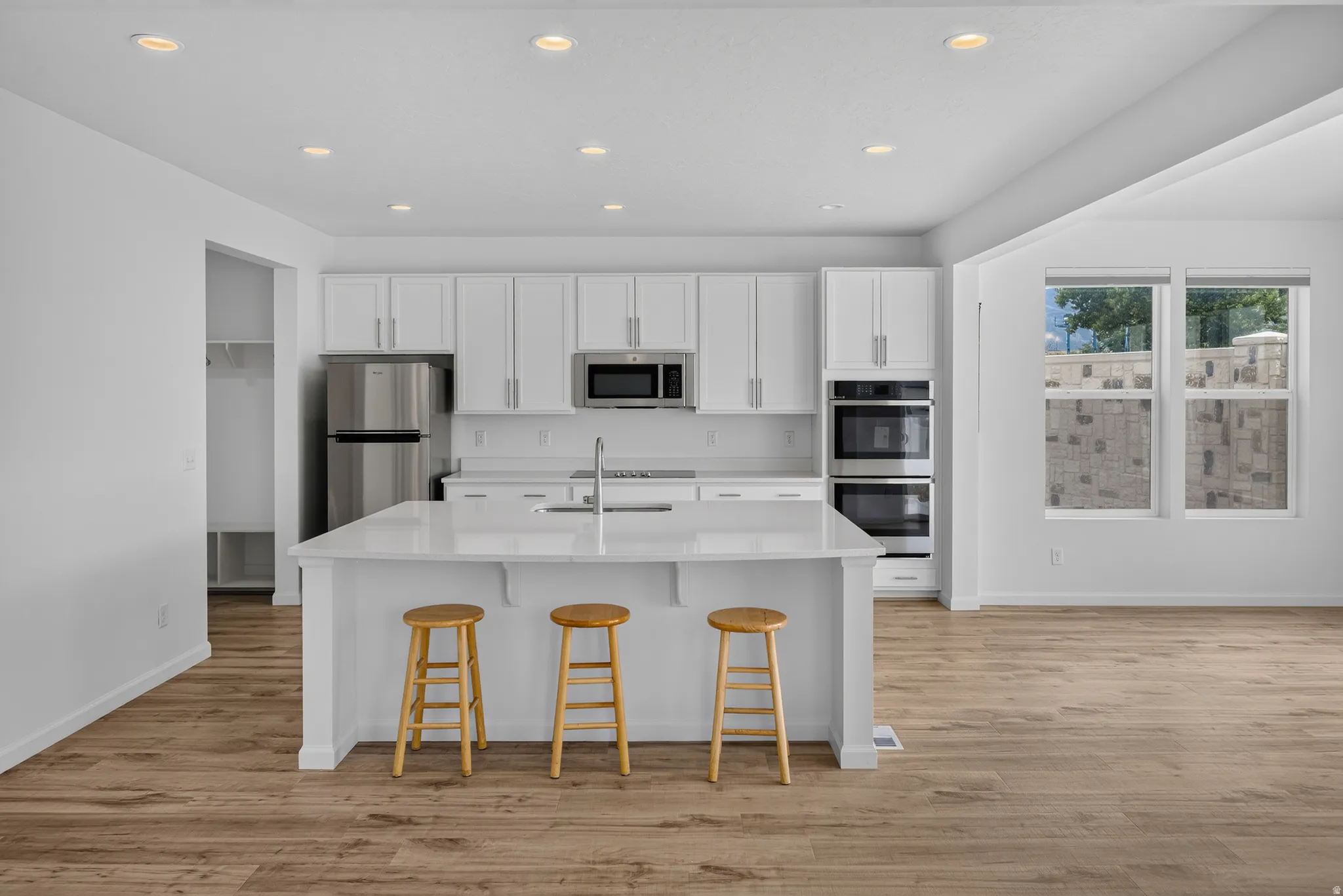 Open-concept kitchen featuring an island with counter seating, stainless steel appliances, white cabinetry, and wood-finish flooring
