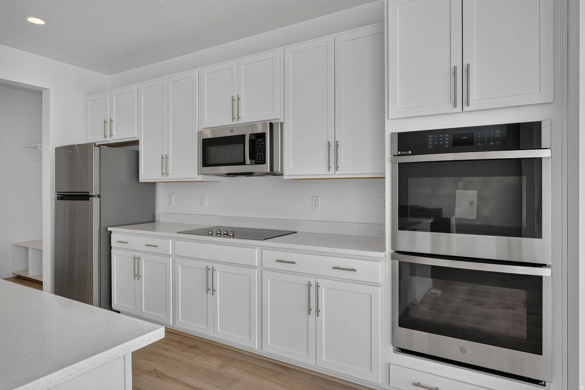 Modern kitchen featuring white shaker cabinetry, stainless steel appliances, a built-in double oven, sleek cooktop, and light-toned countertops