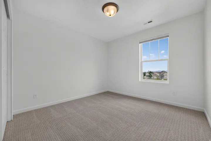 Bright interior featuring neutral carpeting, white walls, a single window, and a ceiling-mounted light fixture
