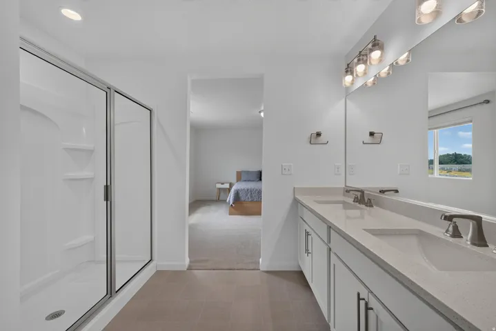 Bathroom featuring a double vanity with light-toned countertops and undermount sinks, a glass-enclosed shower with integrated shelving, and tiled flooring