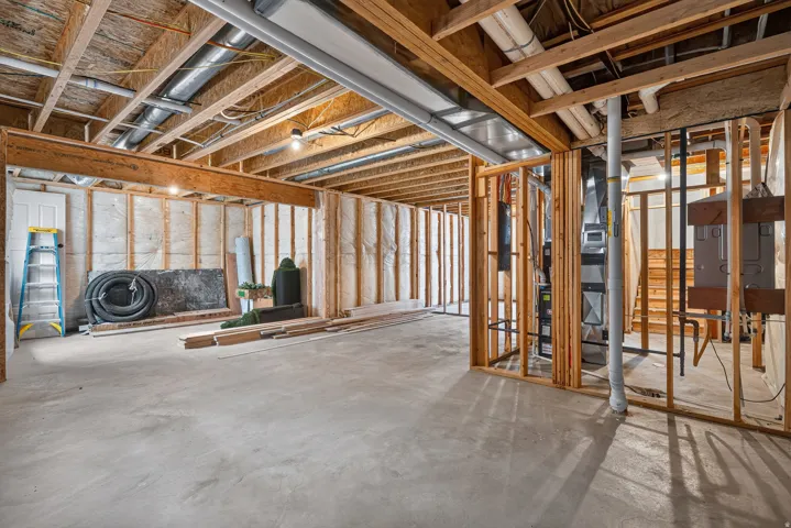 Unfinished basement with concrete flooring, exposed wooden joists, and framed walls