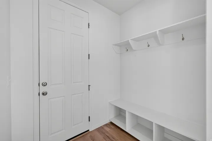 Functional entryway featuring wood-finish flooring, a white paneled door with polished hardware, and a built-in storage bench with open cubbies