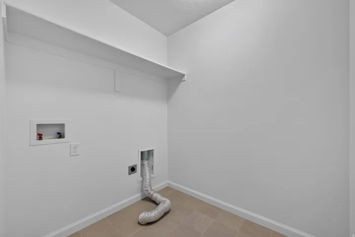 Dedicated utility space featuring a wall-mounted shelf, light-toned tile flooring, and integrated laundry hookups