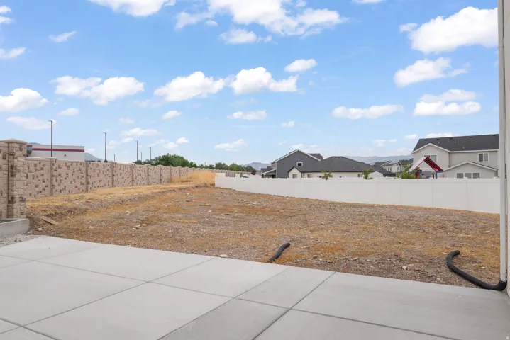 Expansive concrete patio overlooking a vacant lot, framed by a patterned stone wall on one side and a white privacy fence on the other
