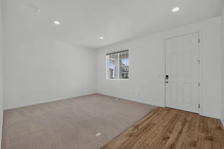 Bright interior space featuring wood-finish flooring at the entry, neutral carpet, and recessed lighting