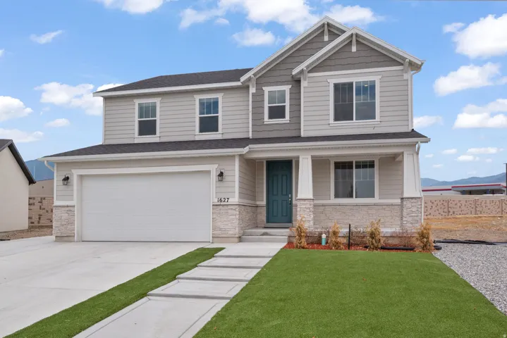 Two-story residence featuring light gray siding, stone veneer accents, and a dark teal entry door
