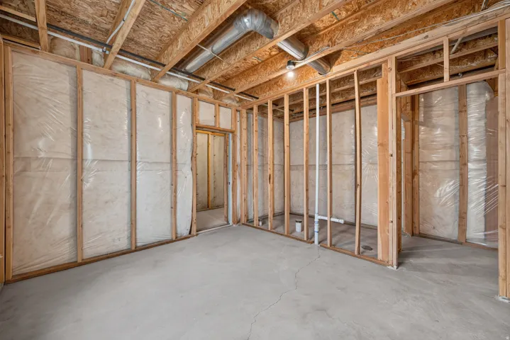 Unfinished basement space featuring exposed wooden framing, concrete flooring, insulation with vapor barrier, and exposed ductwork