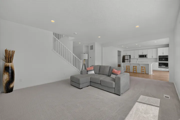 Open-concept living area featuring light-colored carpeting, recessed lighting, and a white staircase with wood railings