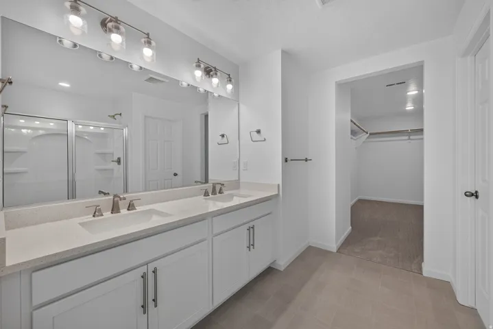 Dual vanity featuring integrated sinks and brushed nickel faucets, quartz-finish countertop, white shaker-style cabinetry, and a full-width mirror with overhead light fixtures