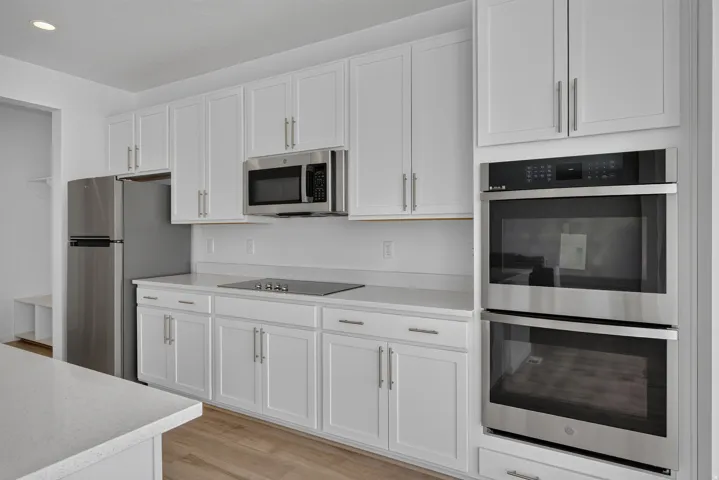 Modern kitchen featuring white shaker cabinetry, stainless steel appliances, a built-in double oven, sleek cooktop, and light-toned countertops
