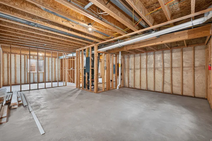 Unfinished lower level featuring exposed wood framing, concrete flooring, visible ceiling joists, and a window with horizontal blinds