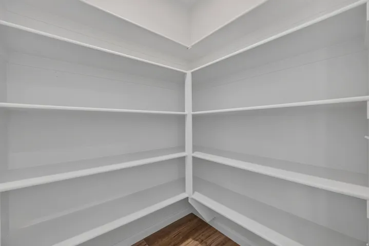 Corner pantry featuring multiple tiers of white shelving and wood-finish flooring