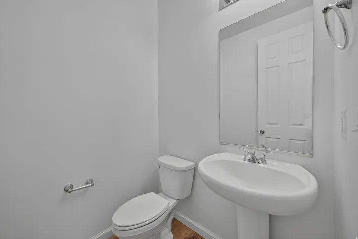 Pedestal sink with chrome faucet, wall-mounted mirror, and wood-finish flooring