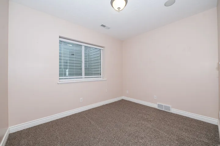 Neutral-toned room with plush carpeting, a single window featuring horizontal blinds, and white baseboards