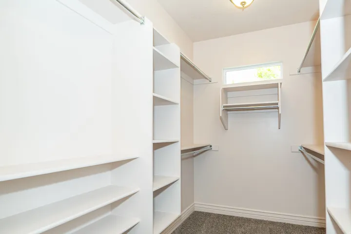 Walk-in closet with integrated white shelving, multiple hanging rods, a transom window, overhead lighting, and gray carpet flooring