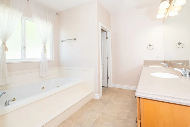 Bathroom featuring a built-in jetted tub, dual window, a double vanity with integrated sinks, and tiled flooring