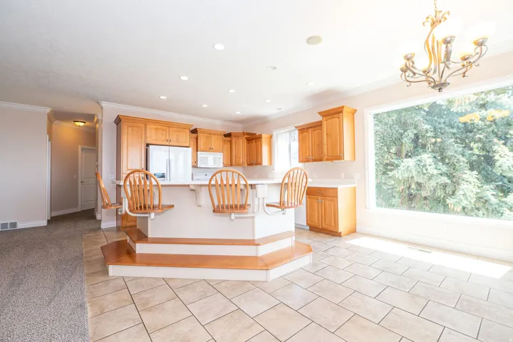 Open-concept kitchen featuring light wood cabinetry, white appliances, a tiered breakfast bar with integrated seating, and tile flooring