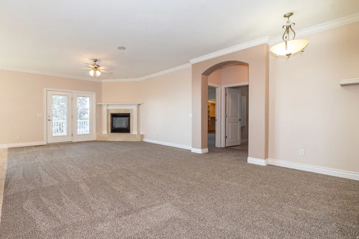 Spacious living area featuring neutral carpeting, a corner fireplace with a white mantel, and double glass doors opening to a balcony