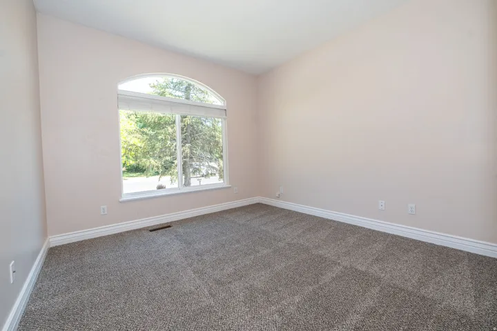 Arched window with broad white trim, neutral-toned walls, vaulted ceiling, plush gray carpeting, and white baseboards