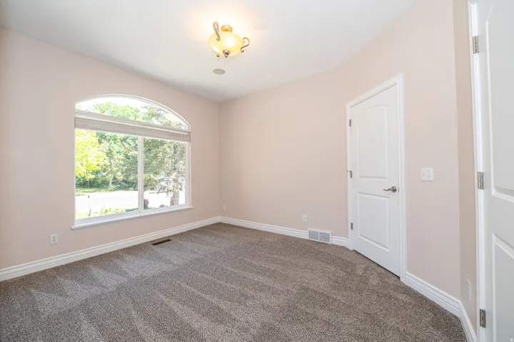 Room featuring an arched window, neutral-toned walls, gray patterned carpeting, white trim, and a white paneled door