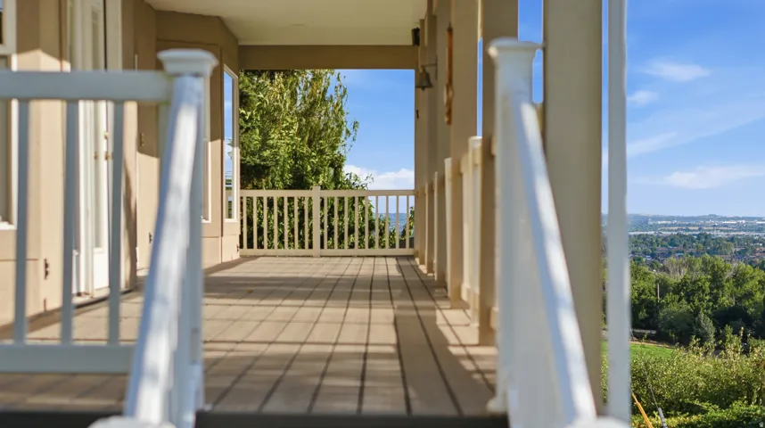 Expansive exterior deck with wood-finish flooring, white railings, and supporting columns