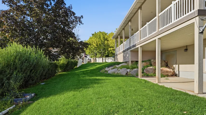 Expansive grassy area with mature landscaping, covered patio, and upper-level deck with white railings