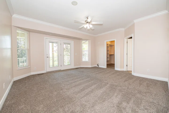Spacious room featuring neutral carpet, crown molding, and a ceiling fan