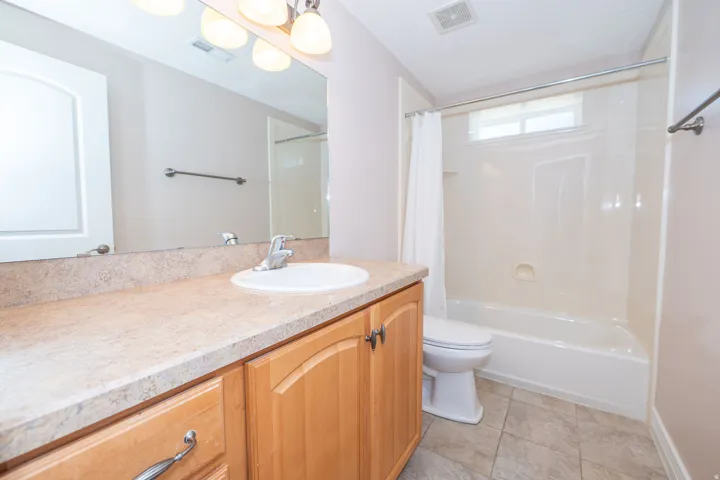 Bathroom featuring a single vanity with wood-finish cabinetry, a large integrated mirror, and a full bathtub with an overhead window
