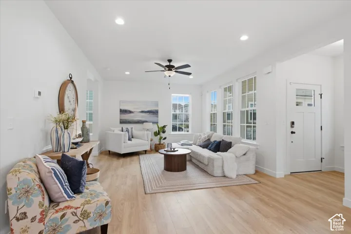 Open-concept interior featuring light wood-finish flooring, recessed lighting, a ceiling fan, and multiple windows with white casing