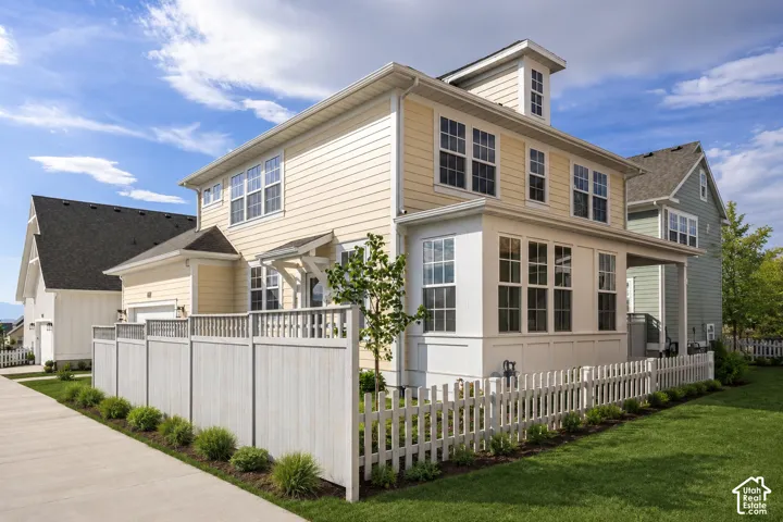 Contemporary residence featuring light yellow siding, a white picket fence, and an expansive side yard with green lawn