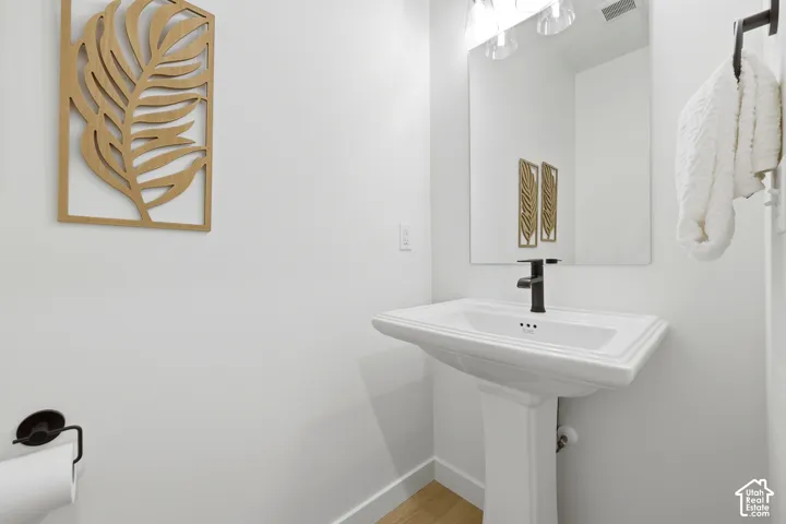 Pedestal sink with a matte black faucet, wall-mounted mirror, and vanity lighting