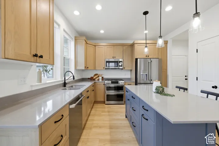 Contemporary kitchen featuring a large central island with a light blue base, light wood-finish cabinetry, light-toned countertops, and stainless steel appliances