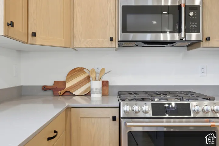 Stainless steel range with a built-in oven, coordinating microwave, light wood-finish cabinetry, and gray countertops