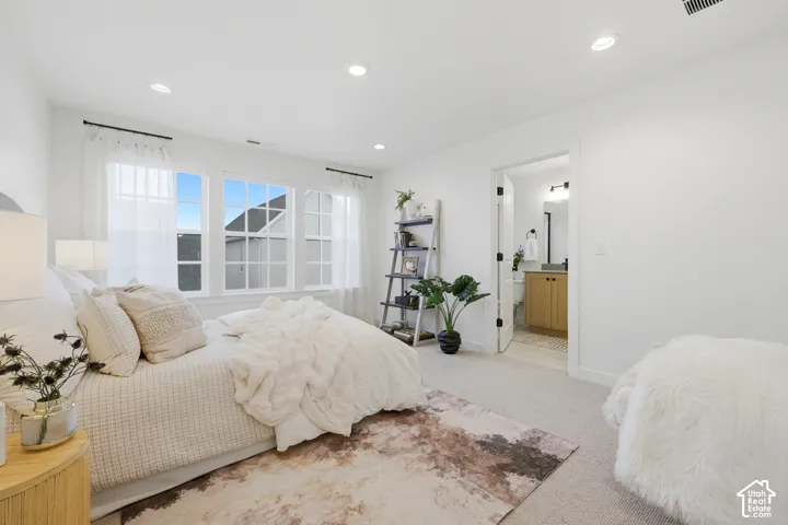 Light-filled interior featuring multiple windows with white sashes, recessed lighting, neutral carpeting, and a visible bathroom entrance with a wood-finish vanity and dark fixtures