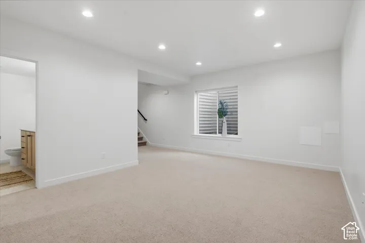 Neutral-toned wall-to-wall carpeting, recessed ceiling lighting, and a window with an integrated egress well
