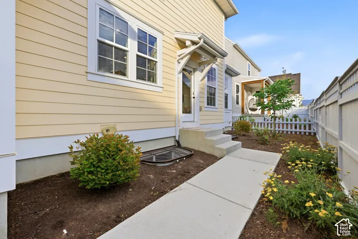 Exterior featuring light yellow siding, white trim windows, a white picket fence, a concrete walkway, and planted landscaping