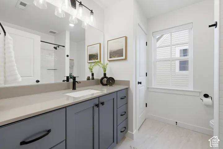 Bathroom featuring a double vanity with grey cabinetry, a light-toned countertop, and undermount sinks