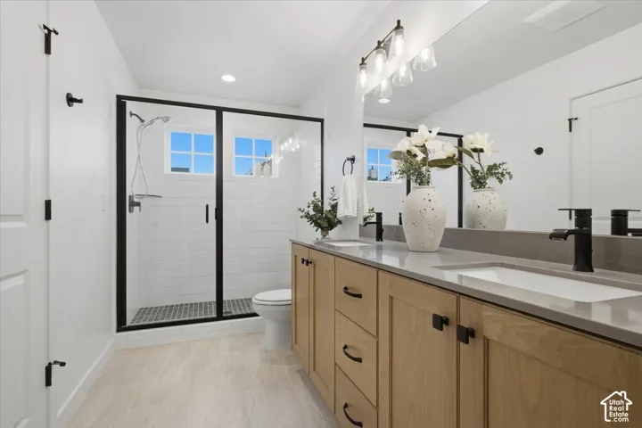 Double vanity featuring light wood-finish cabinetry, quartz countertops, matte black fixtures, and a glass-enclosed walk-in shower with tile surround