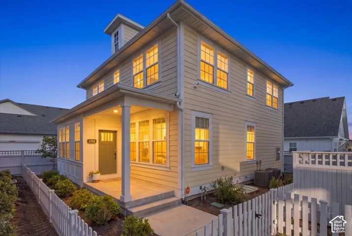 Two-story exterior featuring light-toned horizontal siding, a covered front porch, multi-pane windows, and a classic picket fence