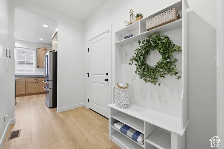 Entryway featuring built-in storage with hooks and shelving, wood-finish flooring, a white paneled door, and recessed lighting