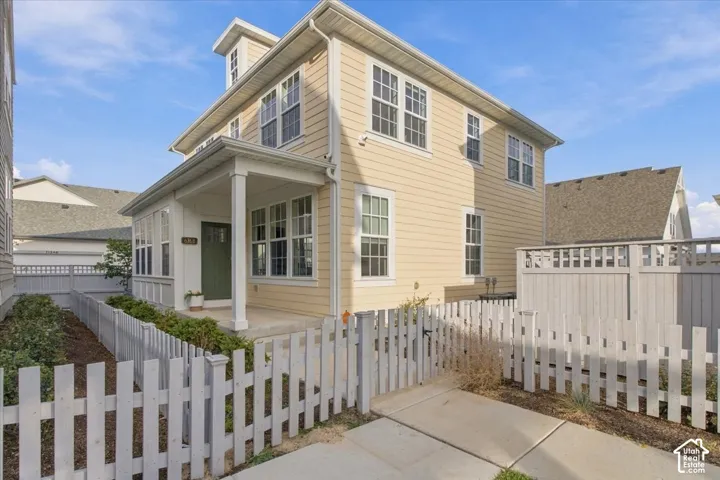 Two-story residence featuring light-colored horizontal siding, a covered front porch with square columns, multiple multi-pane windows, and a white picket fence enclosing the front grounds